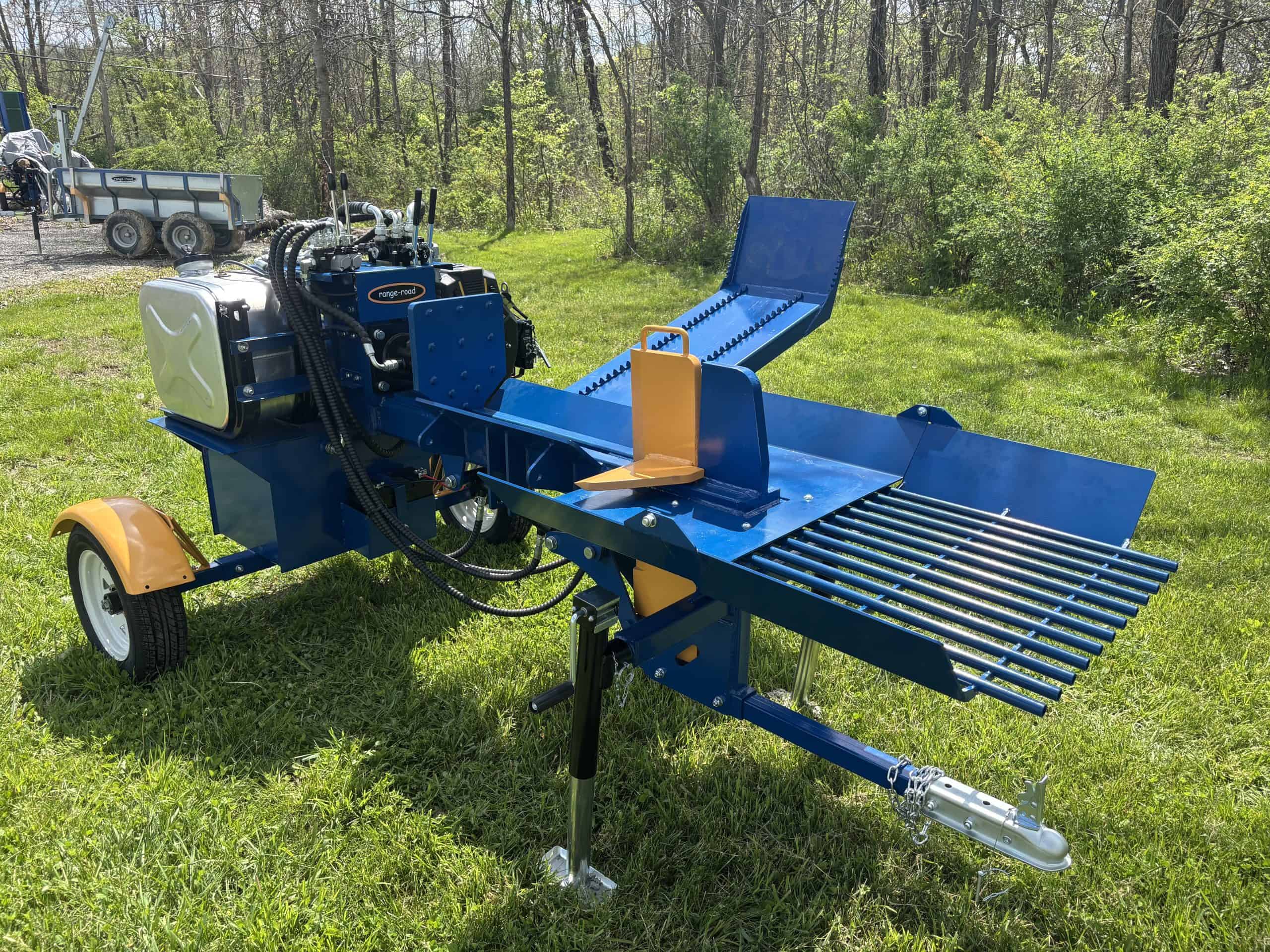Heavy-duty blue log splitter on grassy field with trees in background.